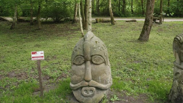 Historic Slavic sculptures in natural woodland setting. Ancient Stone Sculptures in Lush Green Park in Biskupin, Poland. Tilt-up shot.