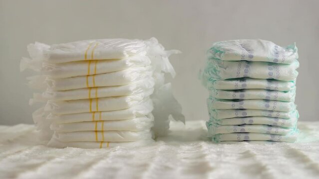 Two stacks of different baby diapers on a white background. A woman's hand runs a feather over diapers. The concept of comfort and dryness for children, close-up