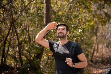 Happy Caucasian man carrying backpack traveling spends free time hiking, walking, exploring, adventure in forest beautiful autumn day, enjoying nature amidst mountains and trees during the weekend.