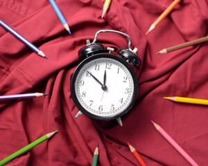Retro alarm clock on red cloths surrounded by colour pencils.