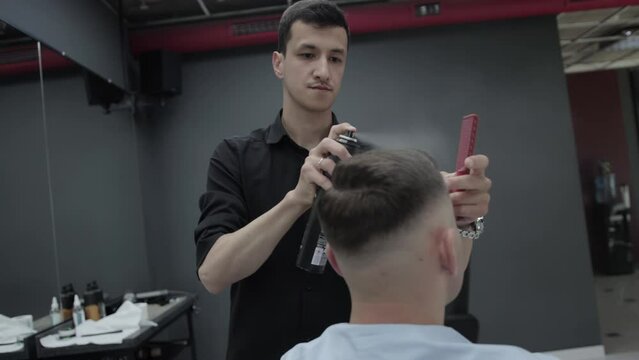 A brunette hairdresser in a barbershop is styling the hair of a male client and spraying it with hairspray. Stylish haircut. Slow motion, fashionable
