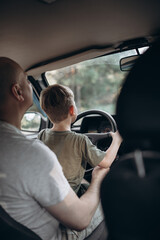 Dad teaches his son to drive a car view from the back