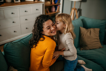 Loving young mother sit on sofa talking chatting with a small preschooler daughter, and little girl child relax on the couch at home, speak enjoy the weekend with her mom or nanny, sharing secrets - obrazy, fototapety, plakaty