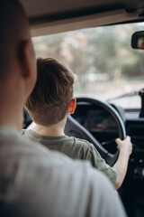 Dad teaches his son to drive a car view from the back