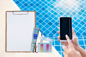 Online report and control for swimming pool water testing, pool maintenance and service, quality water tester, smartphone in girl hand with digital tester on clipboard  on swimming pool edge - obrazy, fototapety, plakaty