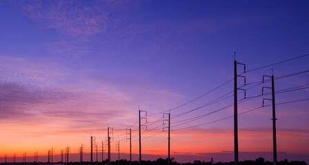 Silhouette two rows of electric poles with cable lines in countryside area against colorful dramatic sunset sky background in panoramic view