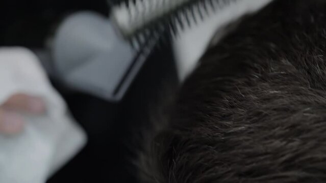A young brunette man is drying and styling his hair with a hairdryer and comb in a hairdresser. Stylish and fashionable haircut in a barbershop. Slow motion, close-up