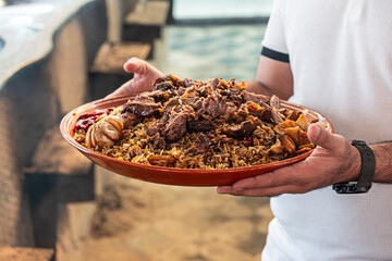 National food - uzbek pilaf with meat in plate with traditional pattern. waiter delivers pilaf in...