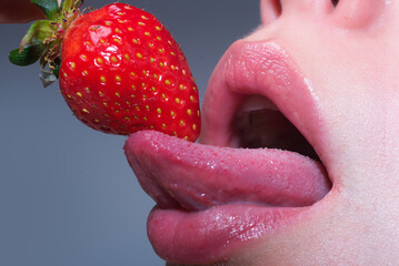 Girl mouth eating strawberry closeup. Sexy open mouth with long tongue lick strawberry. Delicious strawberry. Seductive girl, shiny lip gloss, sexy strawberry. Sexy tongue. Erotic concept. Oral sex. - obrazy, fototapety, plakaty