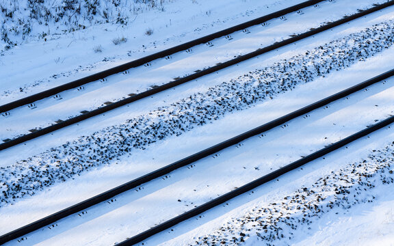 Railway tracks with contrasting snow on german main railroad line with two parallel tracks. Aerial view of infrastructure in winter sunlight. Frosted gravel, screw fixings and thresholds.