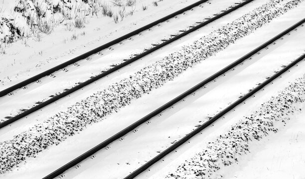 Snow covered parallel railway tracks  on a main railroad line in Iserlohn Sauerland, Germany. Frosted gravel, screw fixings, thresholds. Black and white contrasting infrastructure seen from a bridge.
