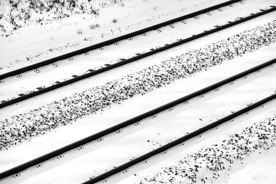 Railway tracks with contrasting snow on german main railroad line with two parallel tracks. Black and white diagonal graphic of infrastructure in winter. Frosted gravel, screw fixings and thresholds.