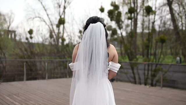 the bride walks in the park in spring from the back with dark hair
