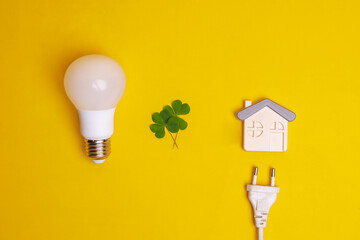 Creative composition flat lay of light bulb, leaf, electric plug and a house symbol on yellow...