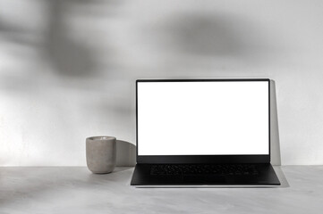 Laptop computer with blank white display mockup, concrete candle on neutral gray marble desk...