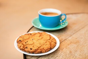 Cup of black coffee and cookie on the edge of a wooden table in a cafe, coffee shop with copy space