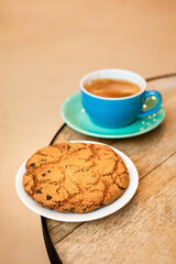 Cup of black coffee and cookie on the edge of a wooden table in a cafe, coffee shop with copy space