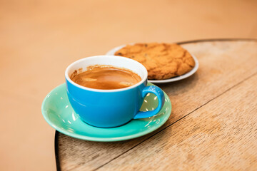 Cup of black coffee and cookie on the edge of a wooden table in a cafe, coffee shop with copy space