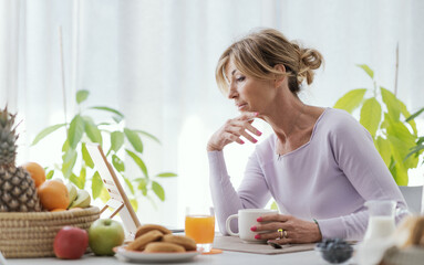 Mature woman having breakfast and using her tablet