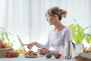 Mature woman having breakfast and using her tablet