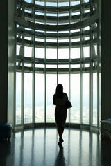 Fototapeta na wymiar Silhouette of woman standing and looking out window with city view background.