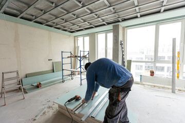 Construction worker assemble a suspended ceiling with drywall and fixing the drywall to the ceiling...