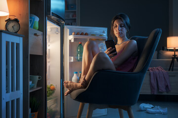 Woman suffering from the heat and sitting in front of the open fridge