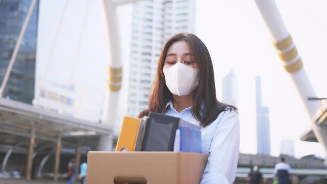 Portrait of young Asian woman wearing covid-19 protective face mask holding box of items after being laid off from job due to coronavirus