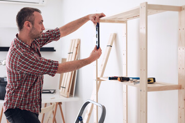 Man assembling new wooden shelf and furniture in the apartment.