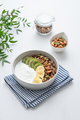 Granola with banana and kiwi on a white table with a green branch.