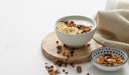 Granola with banana and nuts on a wooden board on a white table with a napkin.