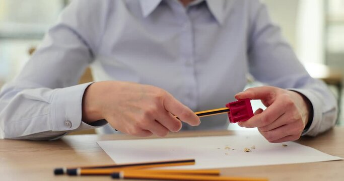 Woman sits at table and holds pencil and sharpener