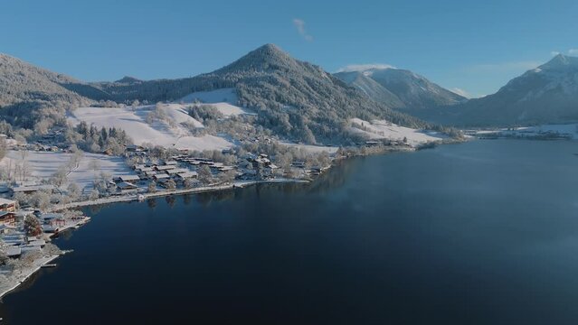 Lake Schliersee with white snow winter landscape, mountains and dark blue water. Traditional old village with a church in Bavaria, Germany.