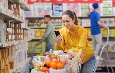 Happy customer doing grocery shopping and using her smartphone