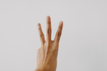 Photo of woman's back hand showing numbers three, counting fingers gesture, isolated on white background wall.