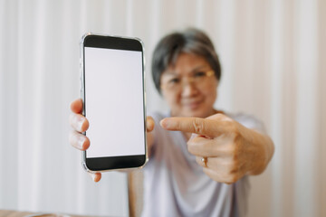 Asian Thai Chinese elder woman holding mobile phone, pointing fingers to white blank screen display.