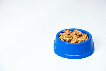 A treat for cats and kittens is a fish-shaped catnip cookie in a blue bowl, copy space for text.