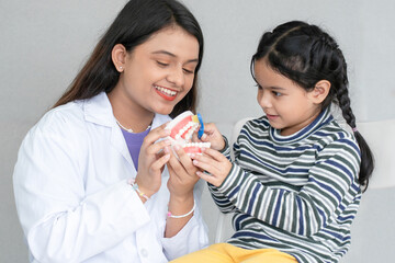 Cute Asian little girl learning how to brush her teeth and gums on a jaw model from young Indian...
