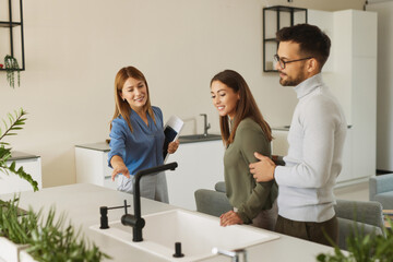 Obraz premium Female shop assistant helping young couple choose new kitchen faucet