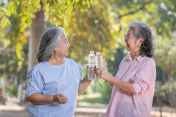 Two elderly Asian women hold water in their hands and look at the camera.