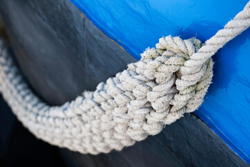 Thick braided rope hangs to the side of a metal ship's hull painted blue. Narrow depth of field