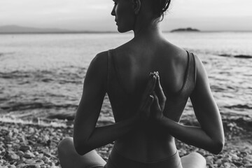 Slender woman practicing yoga on rocky seashore at sunset