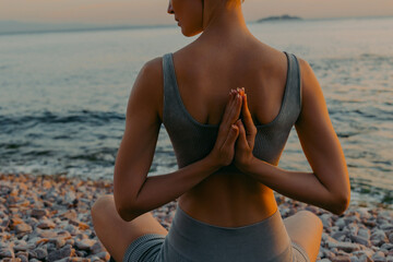 Slender woman practicing yoga on rocky seashore at sunset