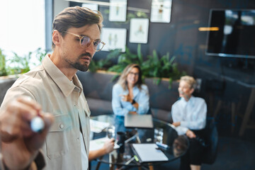 Male team leader writing on a glass wall during his presentation in a business meeting