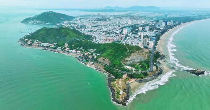 Aerial view of The coastal Vung Tau, Vietnam with many boats, waves, coastline, streets, coconut trees and Tao Phung mountain in Vietnam.