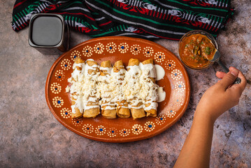 Woman's hand spooning salsa on a plate of golden potato tacos. Mexican food.