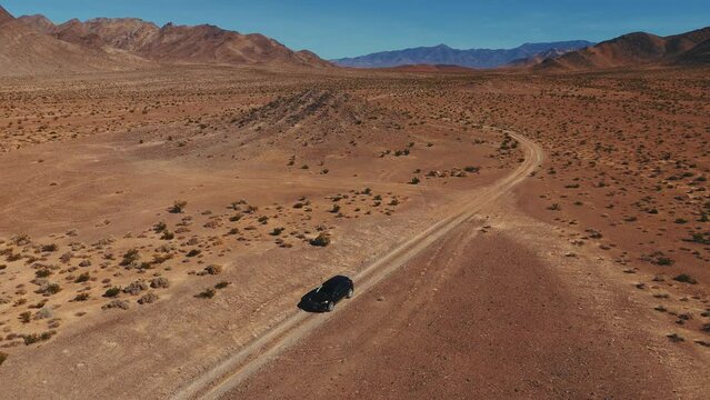Driving a modern black car on desert dirt road off-road in Nevada close to Death Valley. Dry hot Wild West America landscape. Aerial drone