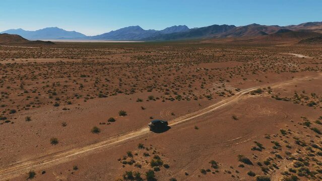Modern black car on desert dirt road off-road in Nevada close to Death Valley. Dry hot Wild West America landscape. Aerial drone
