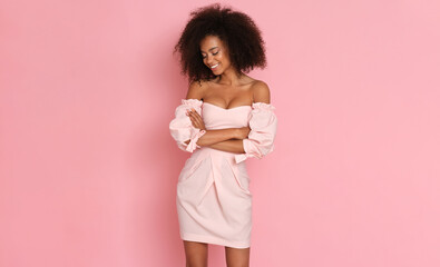 Beautiful afro american woman in a pink dress on a pink background.