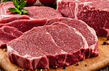 Raw fresh meat Ribeye Steak, seasoning and meat fork on dark background. Fresh raw Prime Black Angus beef steaks on wooden board